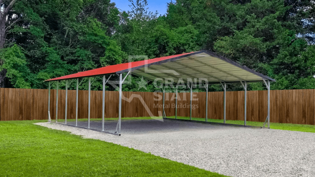 Spacious metal RV carport with a red roof and open design, supported by steel columns, built on a gravel pad in a residential yard surrounded by trees