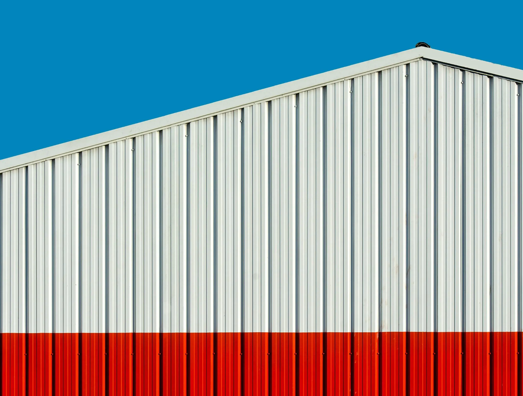 Close-up of a commercial metal building with white corrugated steel panels and a red base under a blue sky